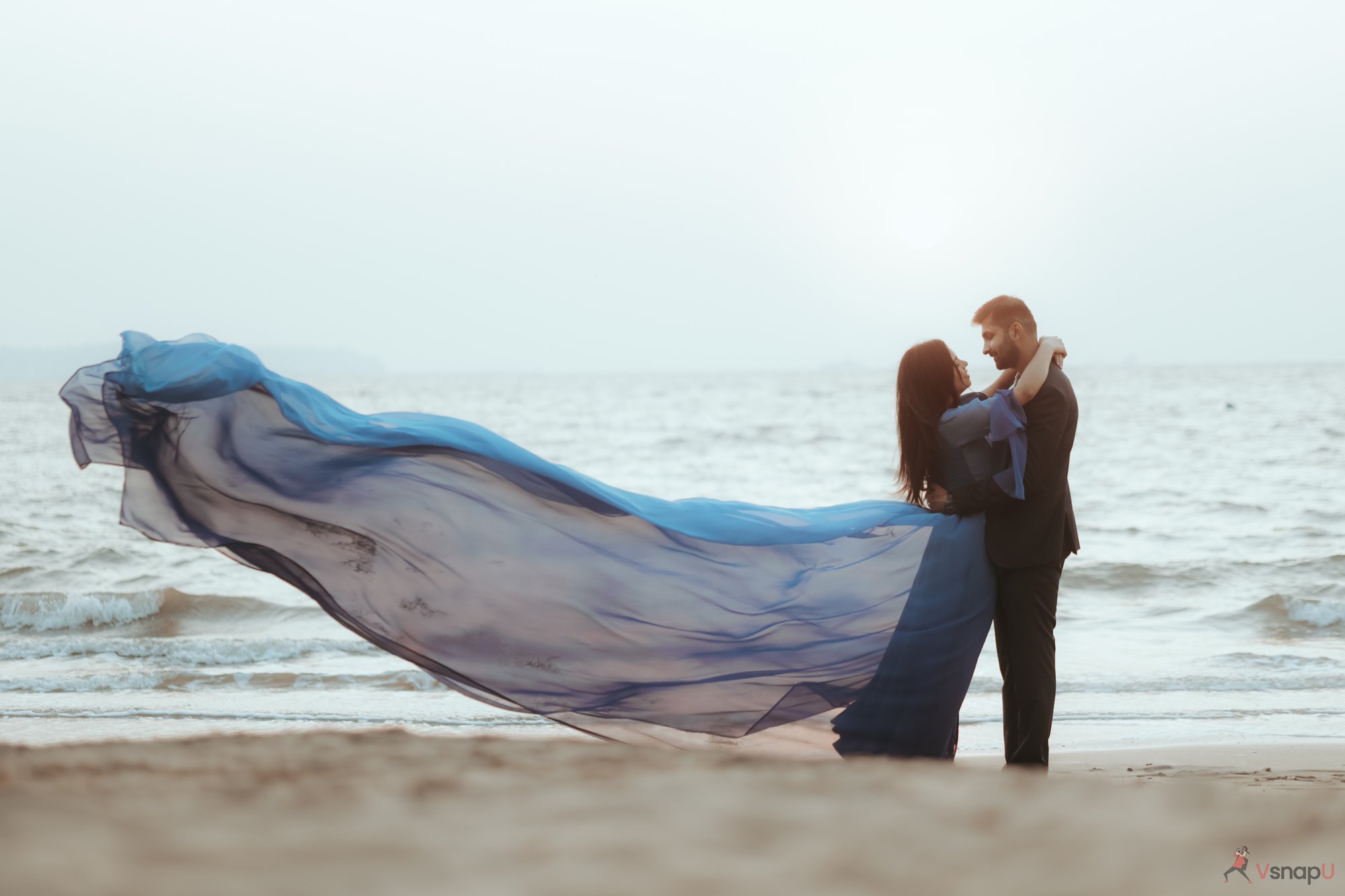 A picture-perfect hug between a bride and groom on the shore.